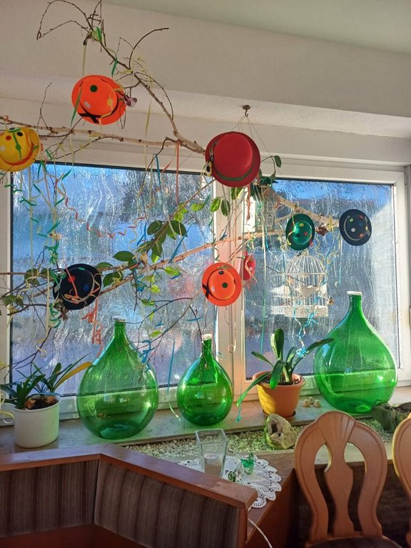 Bild zeigt ein dekoriertes Fenster im Gastraum mit einem Mobilee und gruenen großen bauchigen Flaschen.
