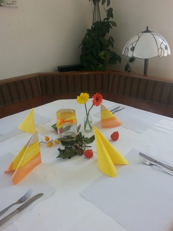 Bild zeigt den runden Ecktisch eingedeckt mit Besteck und gelben Servietten.