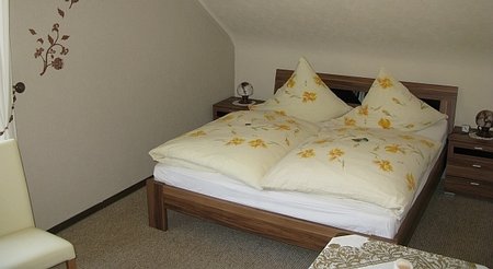 Gästezimmer mit Dachschräge und Doppelbett. Das Bett hat ockergeblümte Bezüge.